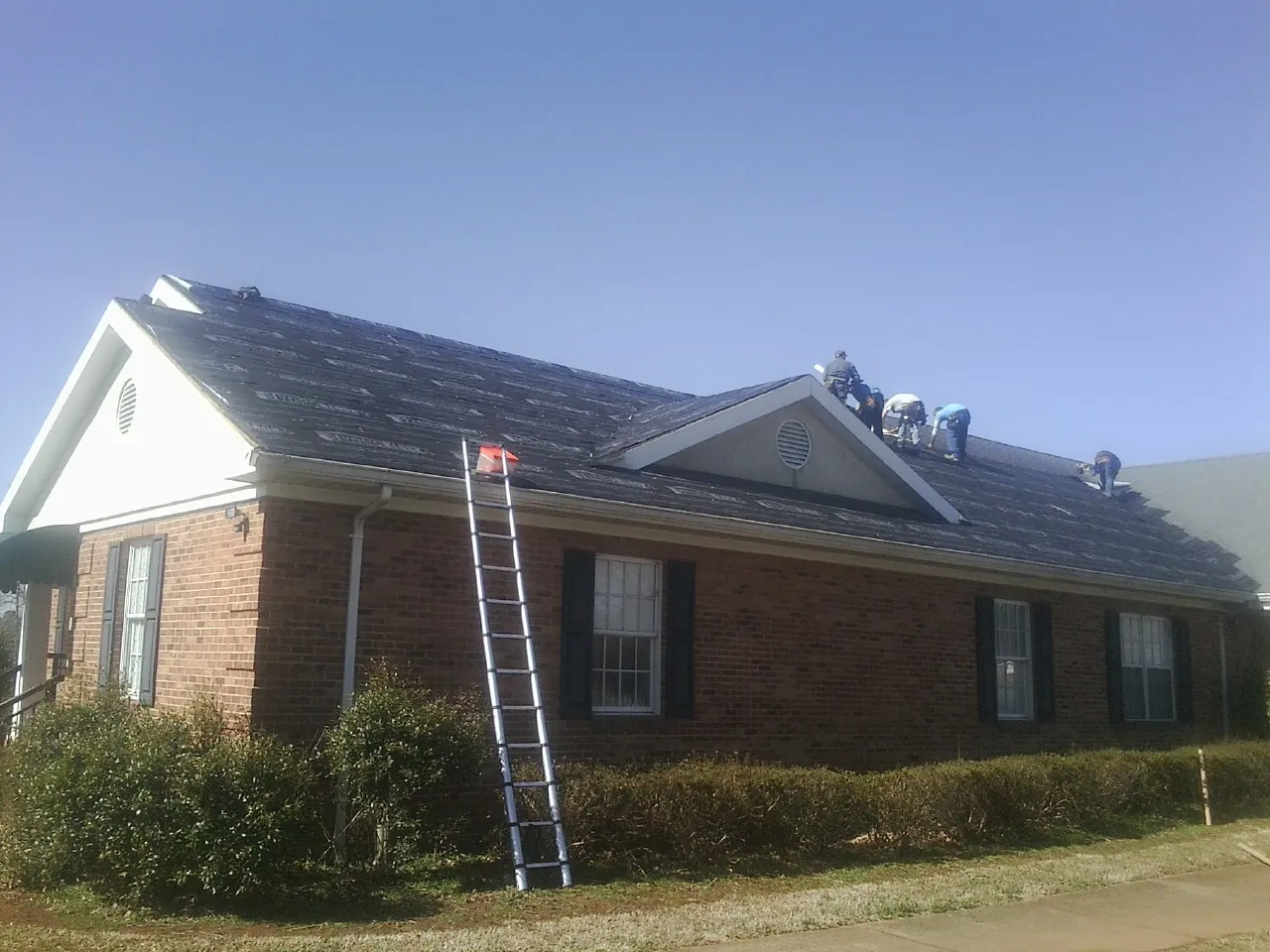 Crew tearing shingles off a brick ranch roof with a ladder set — Emergency Roof Repair work by our crew in Stewart