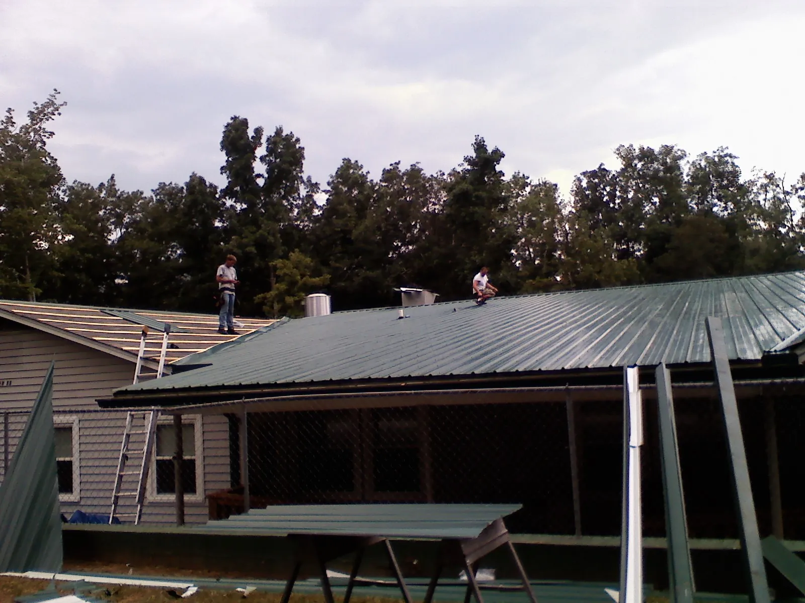 Two roofers installing green metal panels above a covered porch in Stewart
