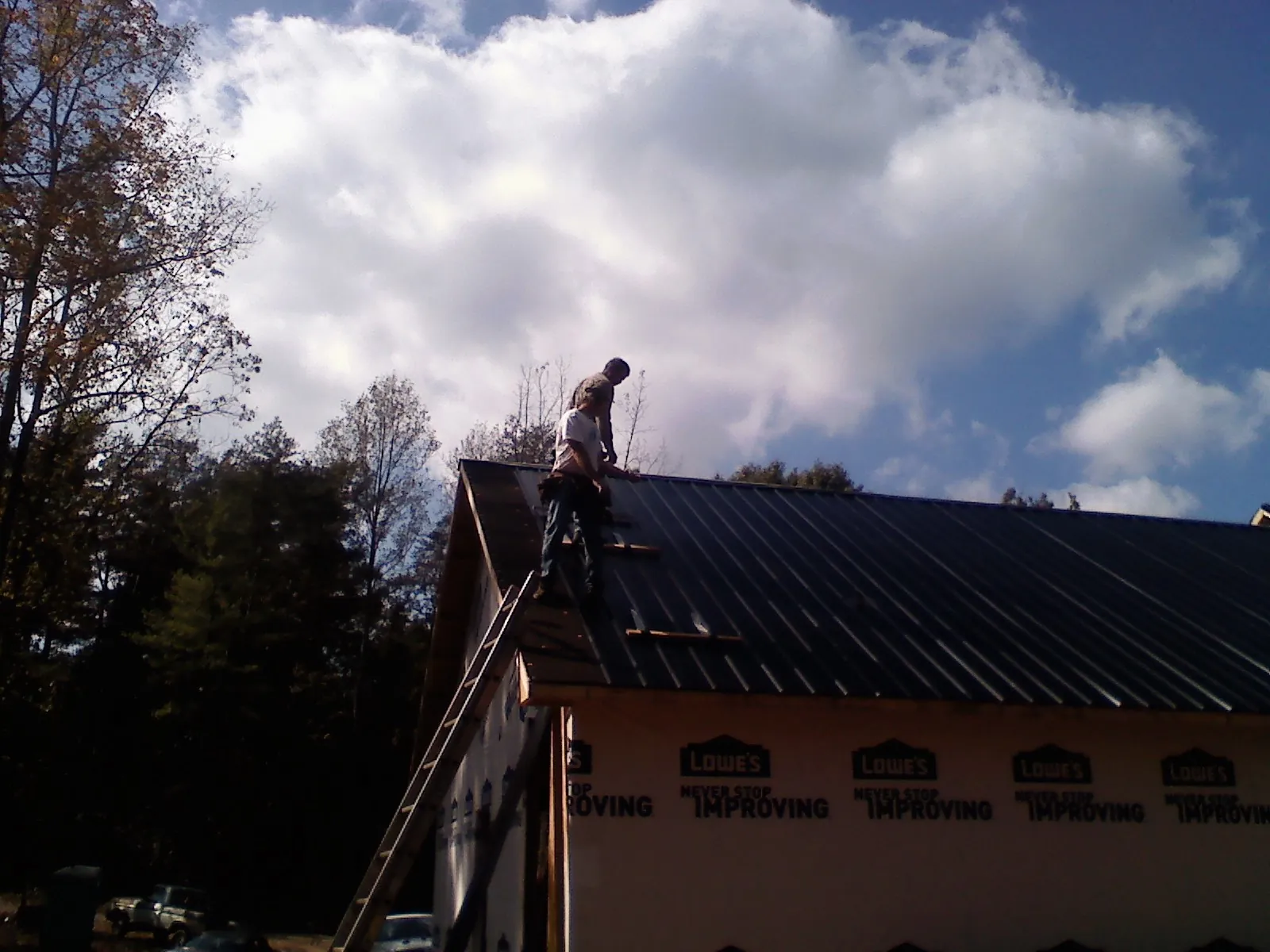 Roofer fastening dark metal panels high against a cloudy sky, from a Roof Inspection job in Stewart