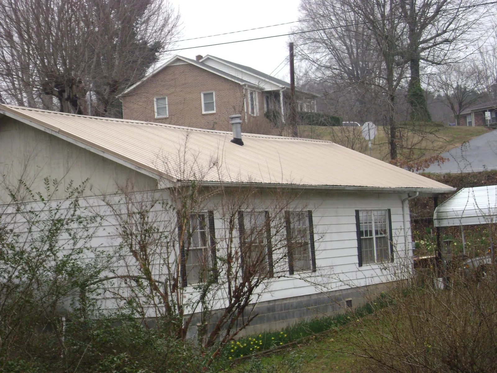 Tan metal roof on a white sided house set into a hillside — Commercial Roofing by Roofing Brothers in Stewart